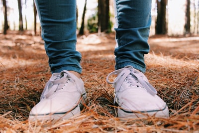 Wearing blue jeans and a white sports shoes standing on the dry leaves
